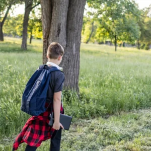 A young boy with a backpack explores a park on a sunny day.