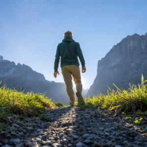 Person hiking on a mountain trail towards the sunlight.