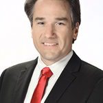 Man in suit with red tie smiling.