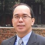 Man wearing glasses and suit outside building.