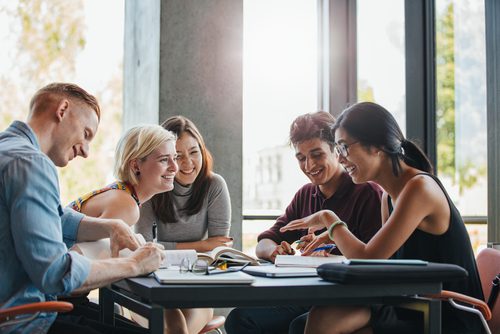 A diverse group of young adults collaborating around a table with laptops and notebooks.