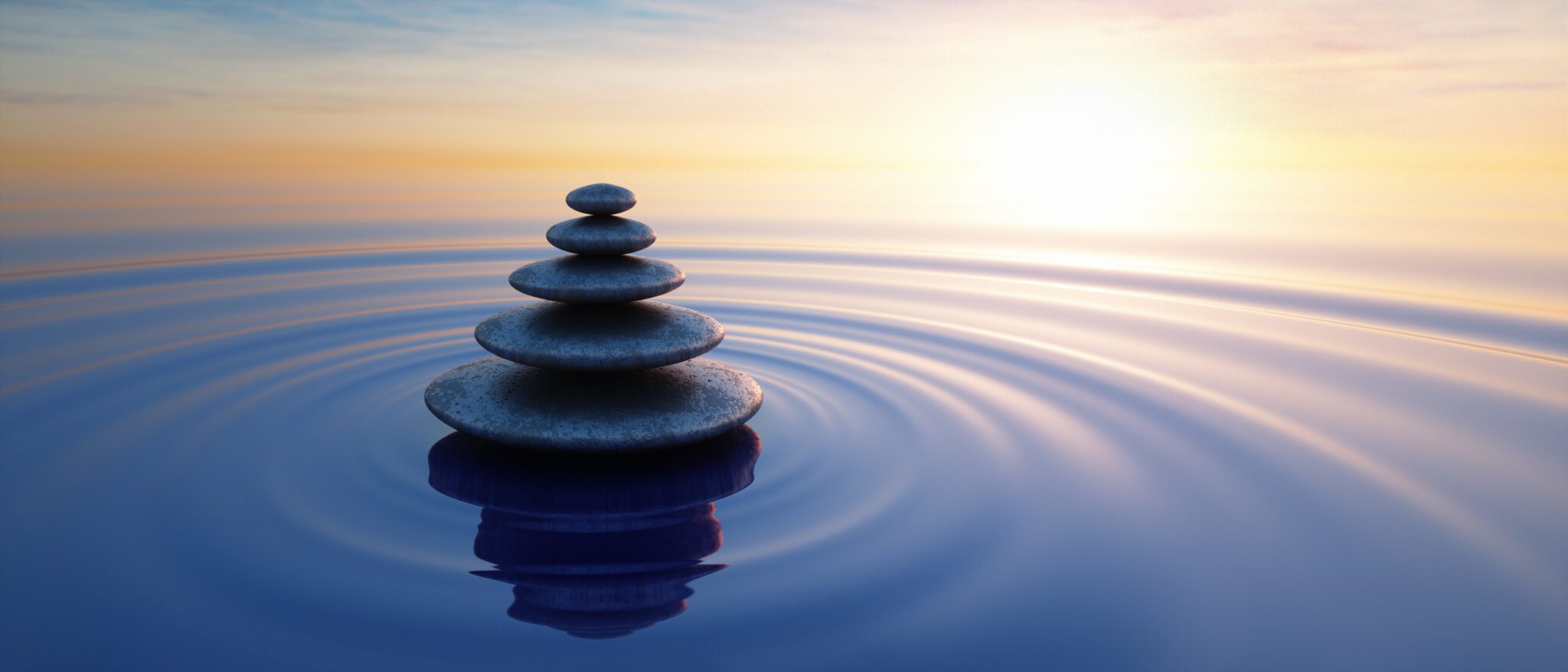 Stacked stones balanced serenely in calm water at sunset.