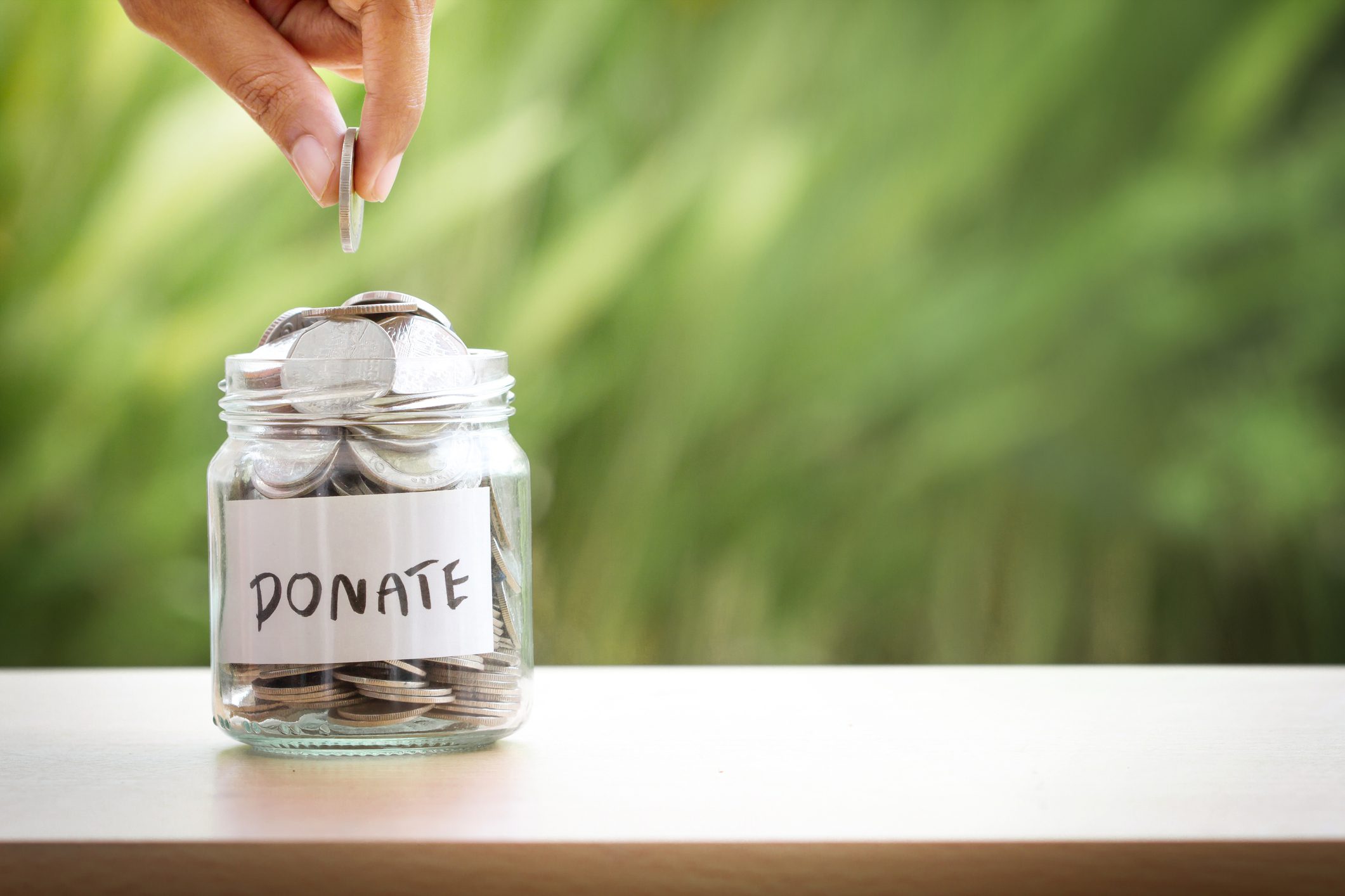 Hand placing a coin into a donate jar filled with coins.