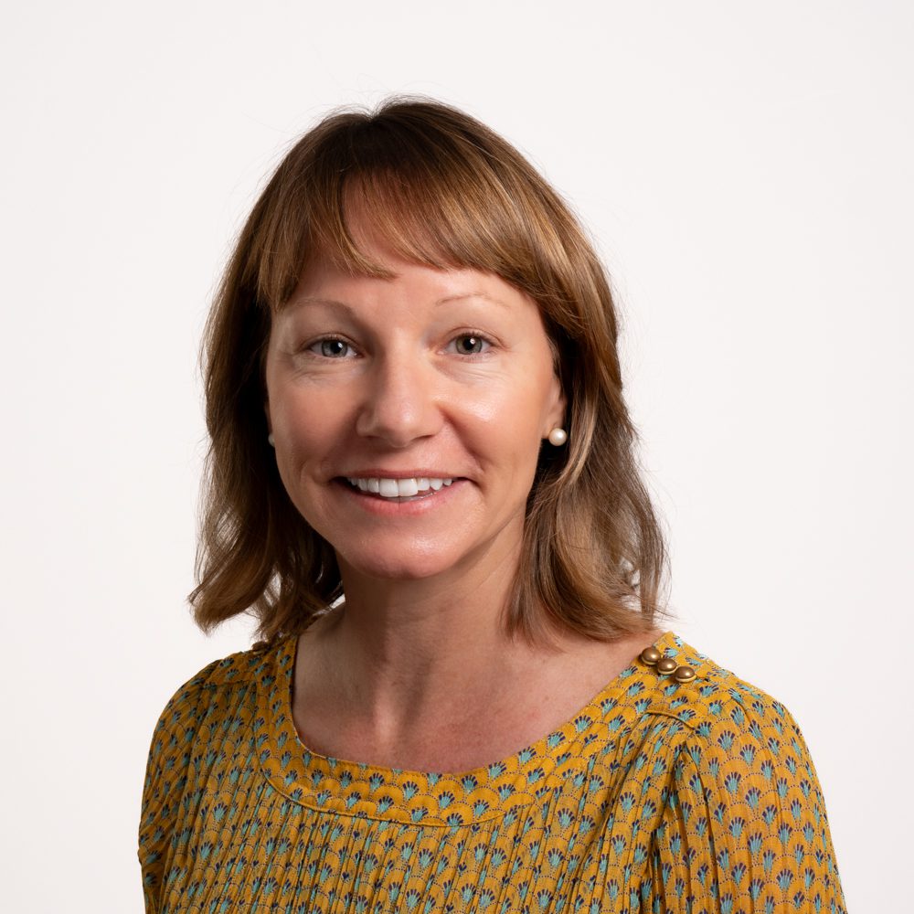 Smiling woman with shoulder-length hair in a patterned top.