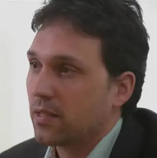 A man with dark hair in a suit looking to the side.