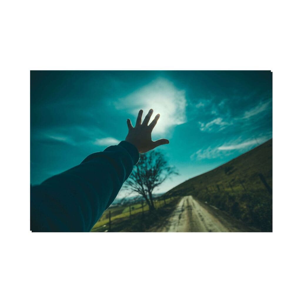 A hand reaching towards the sun in a scenic outdoor setting.