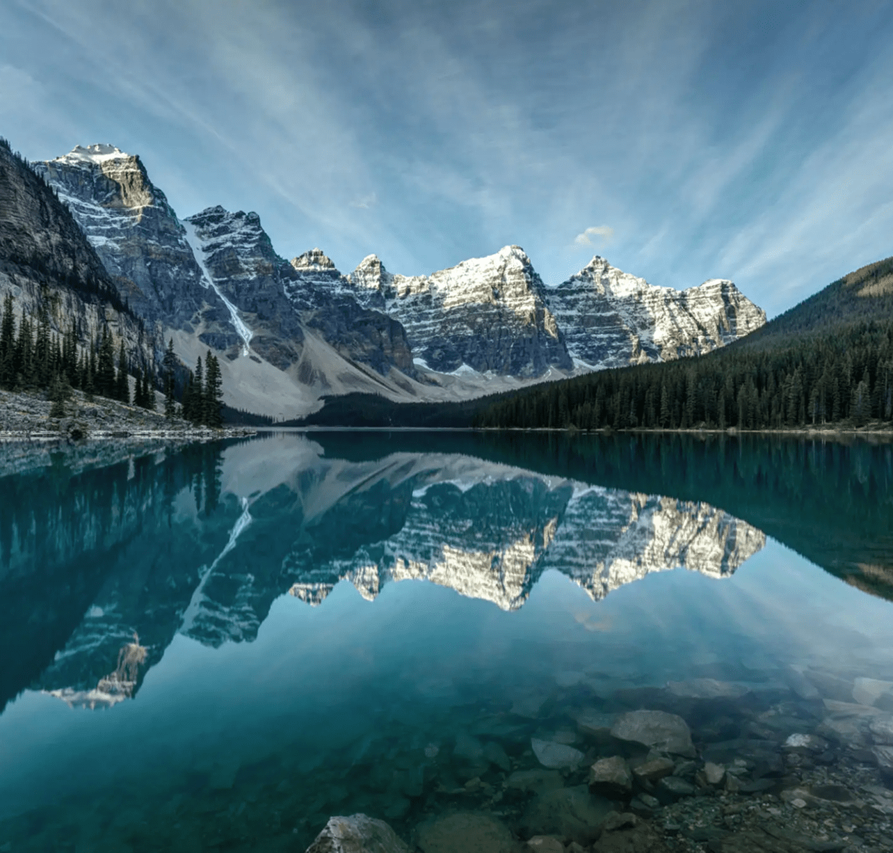 Snow-capped mountains reflect in a crystal-clear lake under a blue sky.