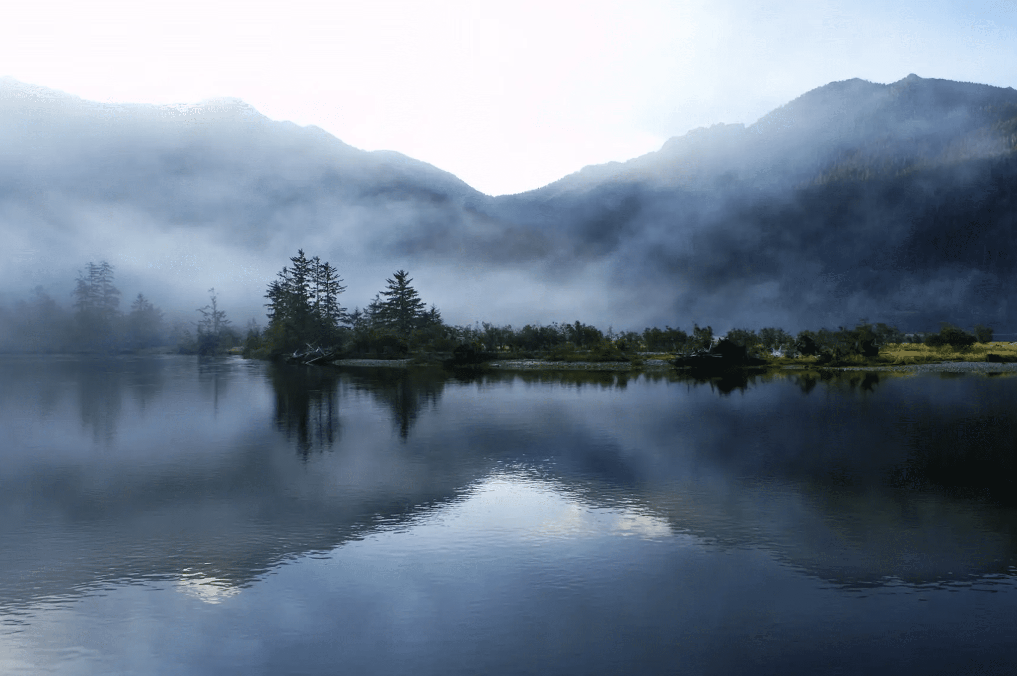 Misty mountains reflecting on a calm lake at dawn.