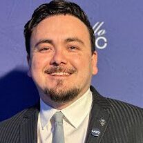 Man in a suit smiling against a blue backdrop.