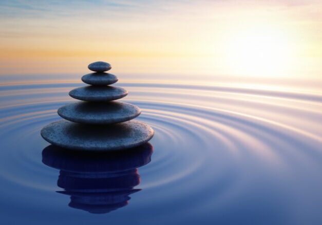 Stacked stones balanced serenely in calm water at sunset.