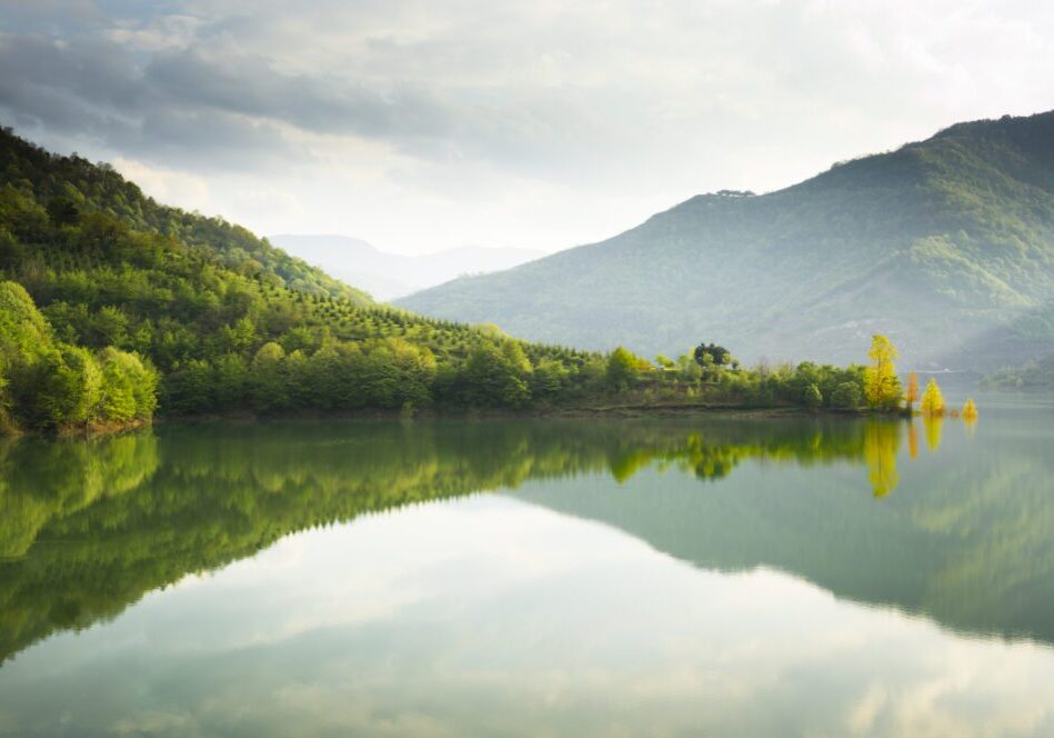 A serene lake reflecting green hills and a cloudy sky.