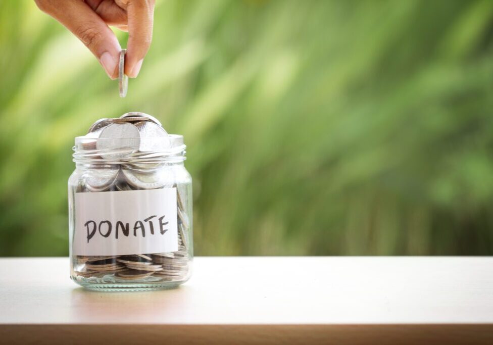 Hand placing a coin into a donate jar filled with coins.