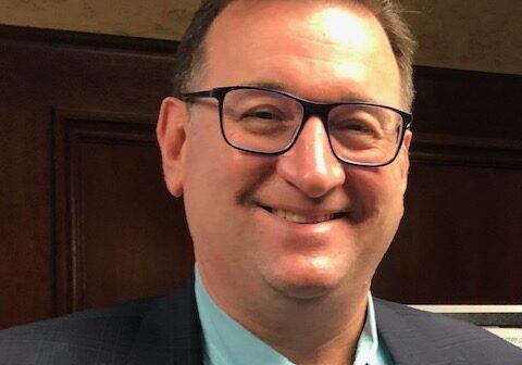 Man wearing glasses and a suit smiling indoors.