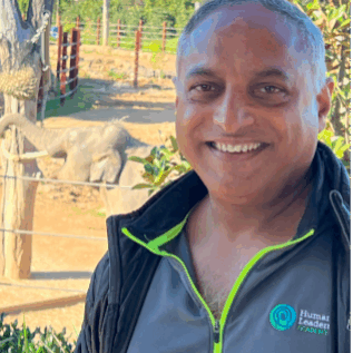 Smiling man outdoors with deer in the background at a park.