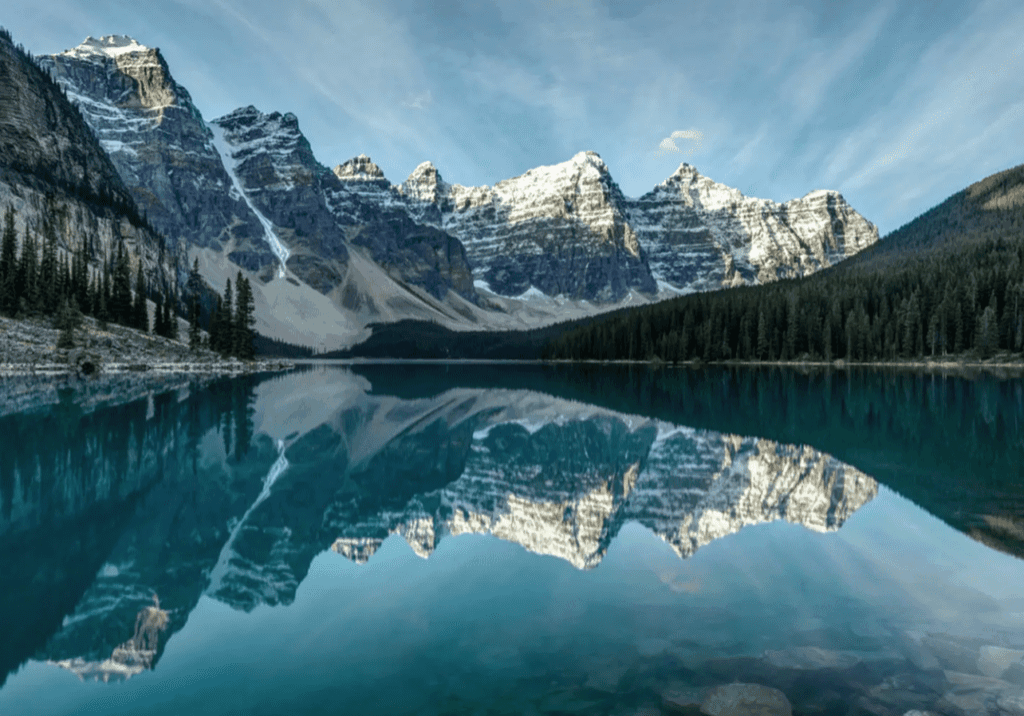 Snow-capped mountains reflect in a crystal-clear lake under a blue sky.
