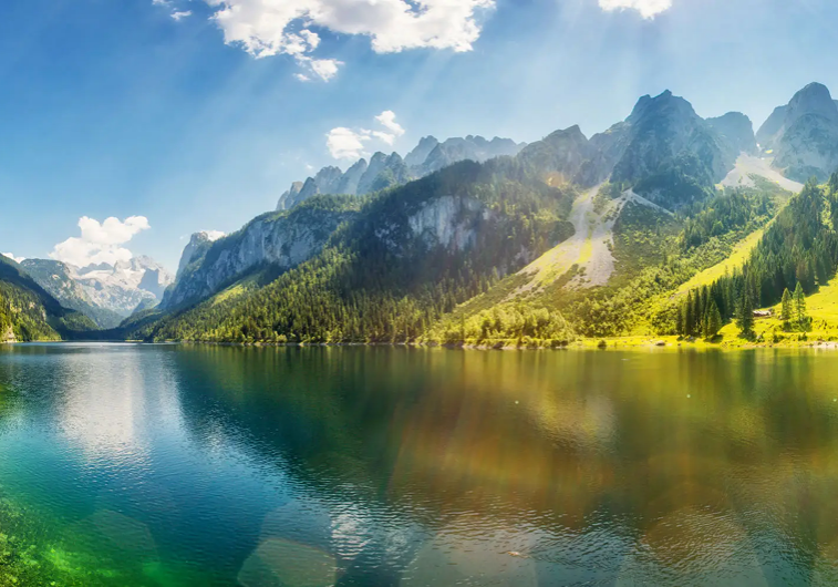 Serene lake reflecting towering mountains under a partly cloudy sky.