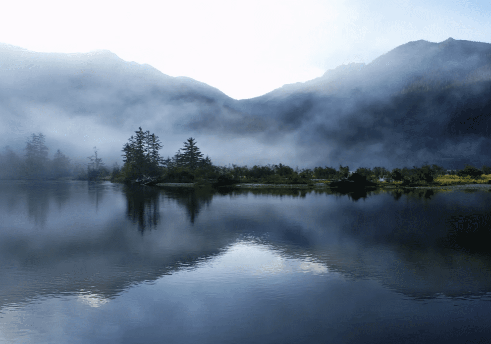 Misty mountains reflecting on a calm lake at dawn.