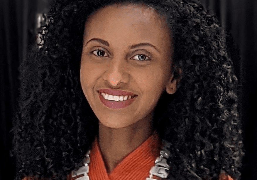 Smiling woman with curly hair and necklace.