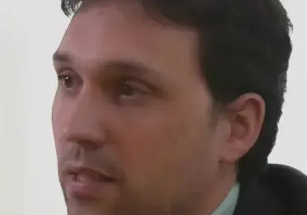 A man with dark hair in a suit looking to the side.