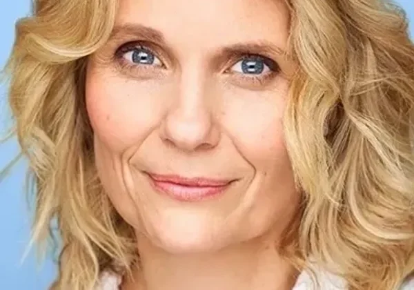 Smiling blonde woman with blue eyes against a blue background.