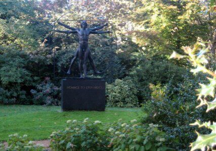 Sculpture of a man with outstretched arms in a garden.